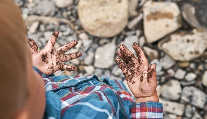 Cute little boy looking on his dirty hands after playing in mud