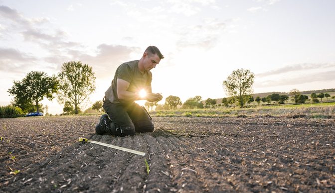 To calculate weeds, a farmer kneels in a rape field and measures with a folding ruler